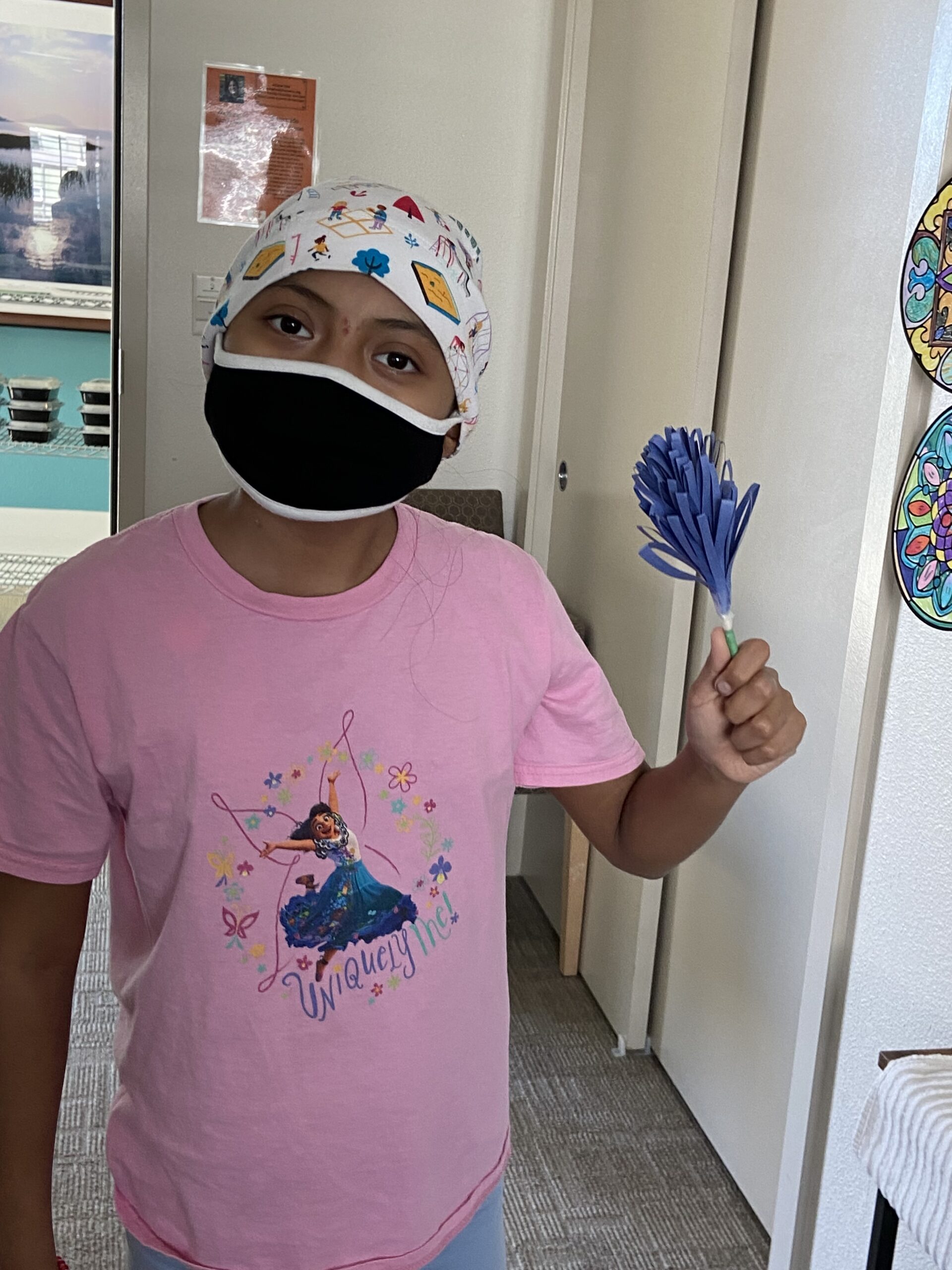13-year-old girl, Zaire, wearing a face mask and holding the blue paper flowers she made 
