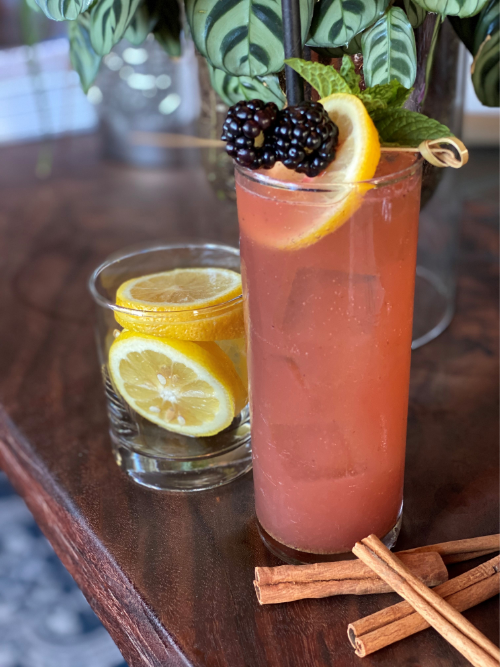 Picture of "Drops of Jupiter Soda" mocktail in a tall glass with pink beverage, lemon garnish, and blackberries