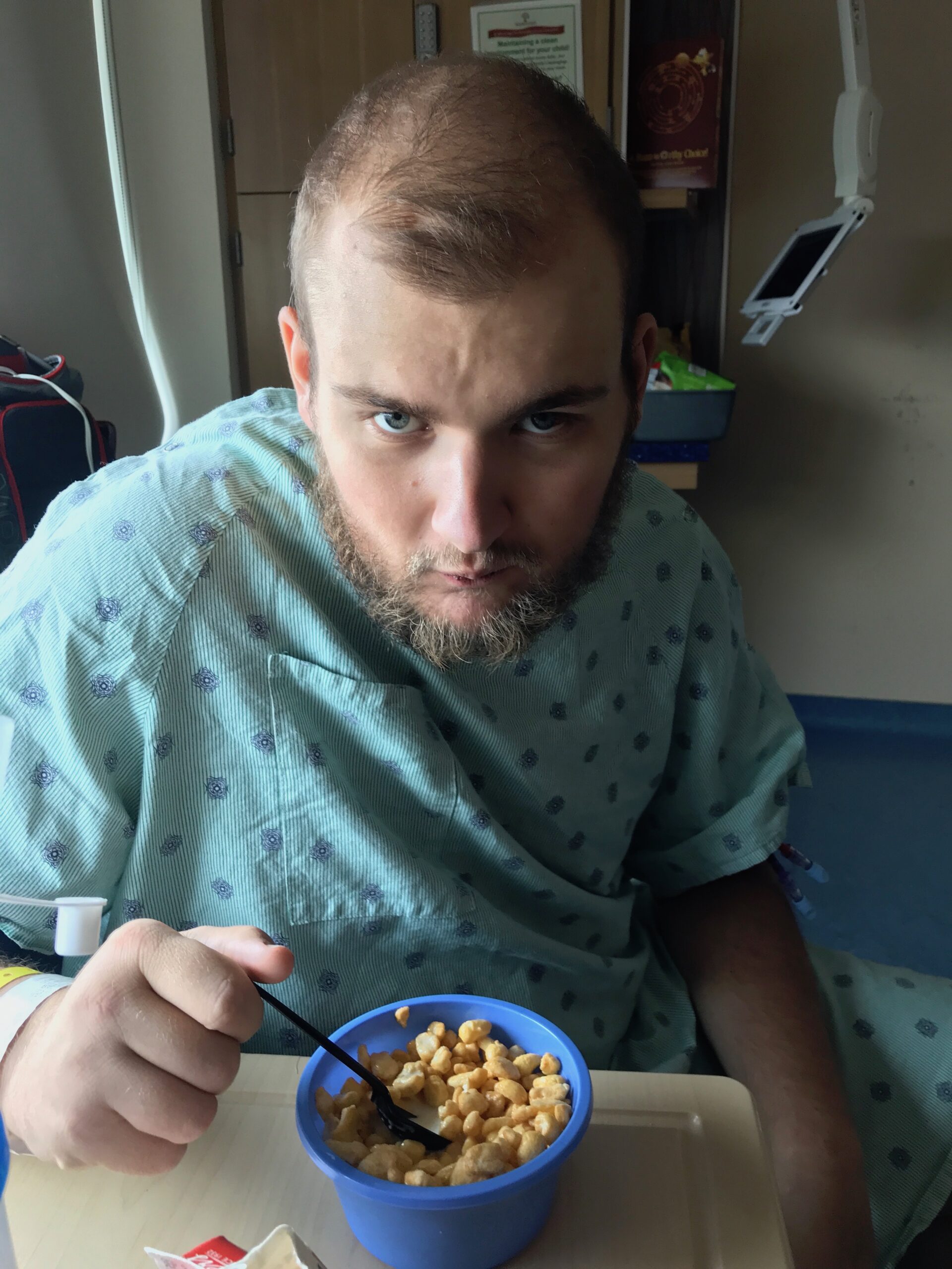 picture of white male name john who is eating cereal from a bowl, dressed in a hospital gown, and beginning to lose his hair from chemotherapy treatment at UCSF Benioff Children's Hospital.