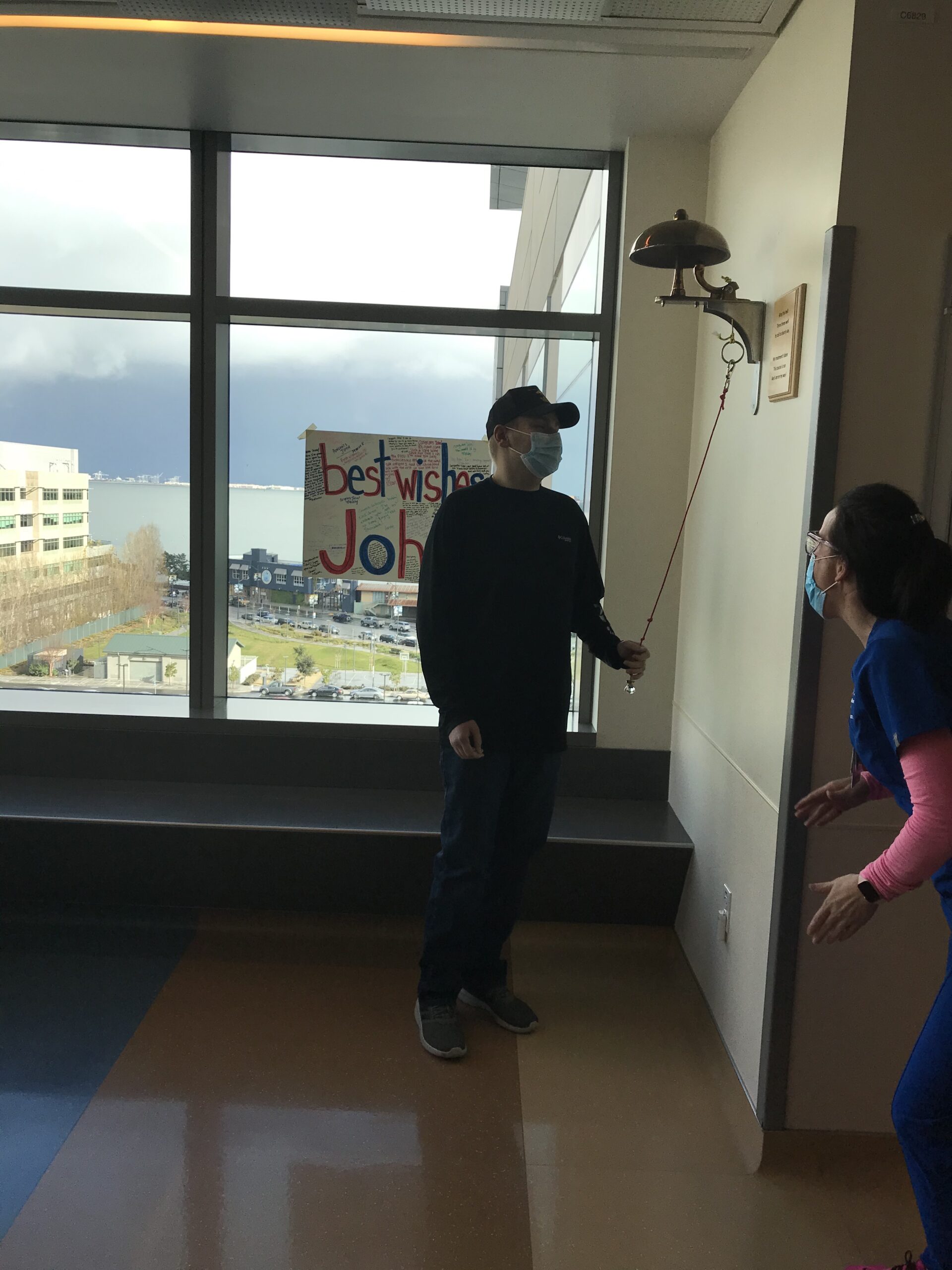 John, a white 22 year old man wearing jeans, a black shirt, and ballcap, rings the bell at UCSF Benioff Children's Hospital.