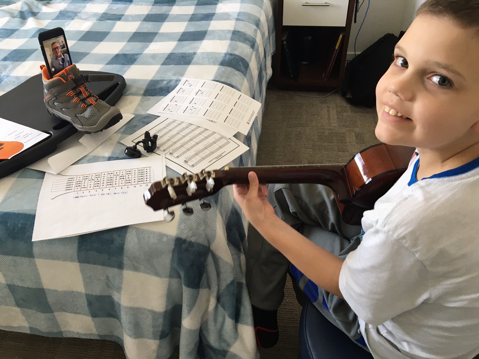 A picture of Sam practicing his guitar with Paul Goold on a mobile phone via video chat 