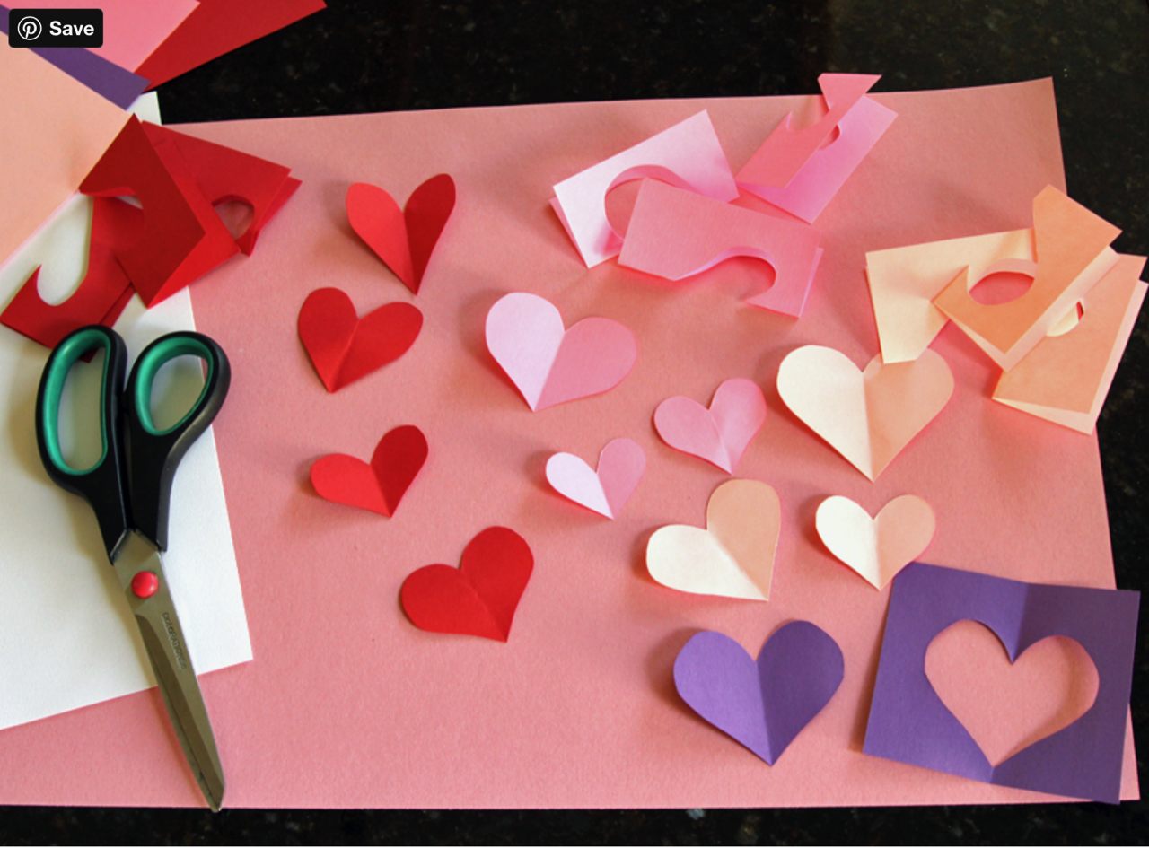 picture of scissors and colored construction paper cut outs into hearts in red, purple, white, and pink for valentines day