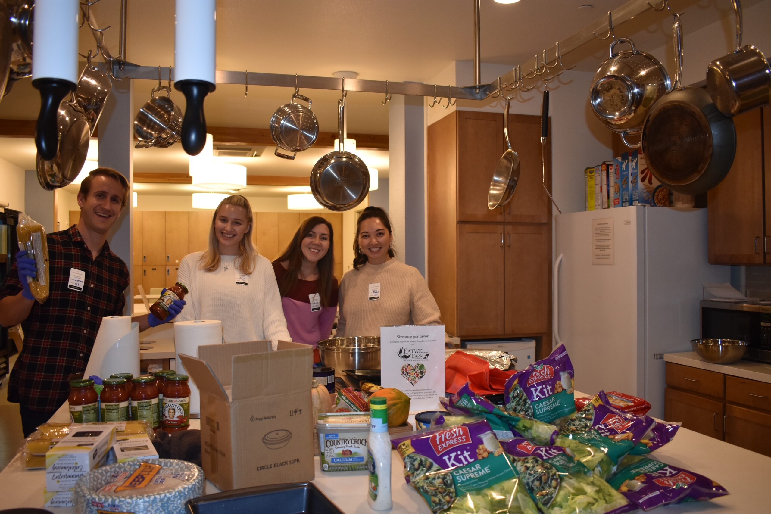 three young women and one young man pose in the kitchen of Family House where they are unpacking groceries to prepare family dinner at Family House.